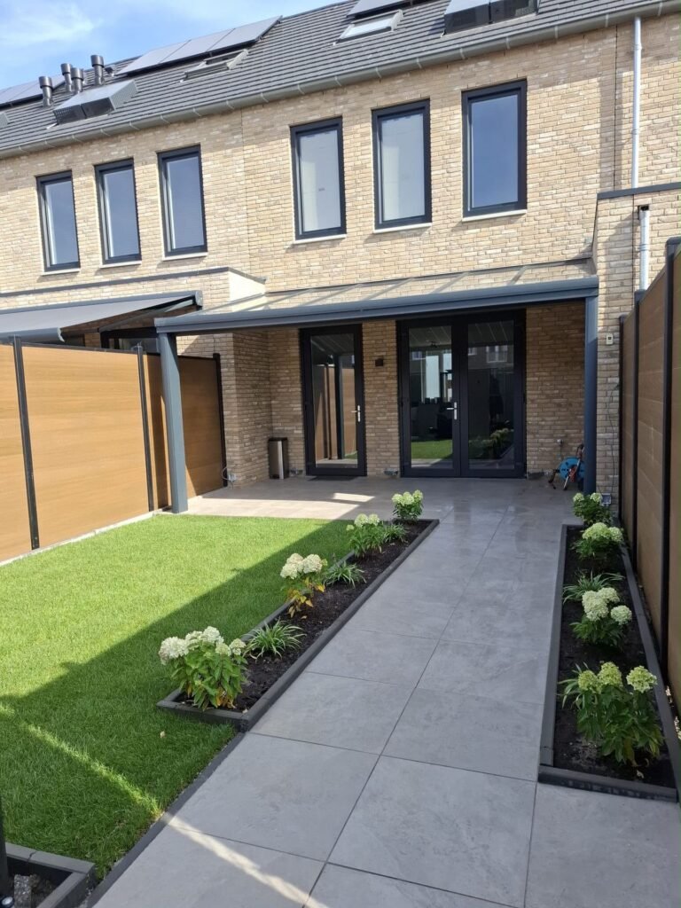 Achtertuin van een nieuwbouwwoning met gazon, tegelpad en borders door Excellent Tuin Onderhoud